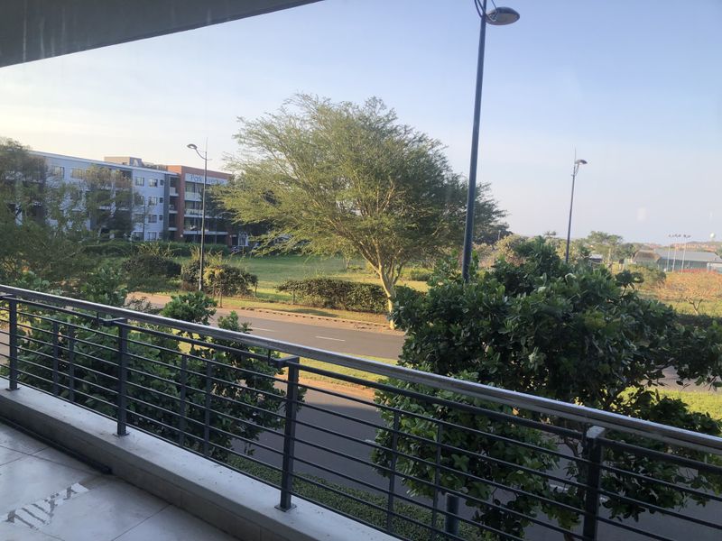 A spacious balcony featuring a modern stainless steel balustrade and tiled flooring, offering an open view of the surrounding neighborhood and greenery.