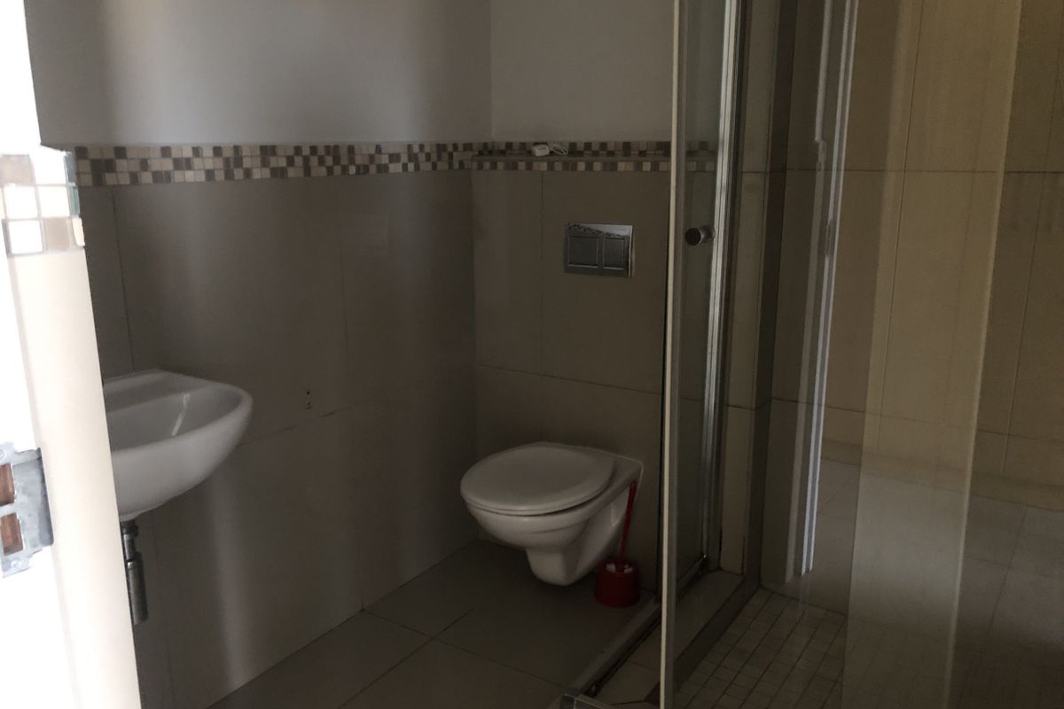 A functional bathroom featuring a wall-mounted toilet, a glass shower enclosure, and a pedestal basin with neutral tiled finishes.