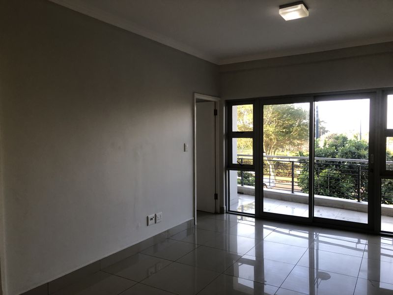 An empty living room featuring large sliding glass doors that open onto a balcony, with neutral tiled flooring and clean wall finishes.