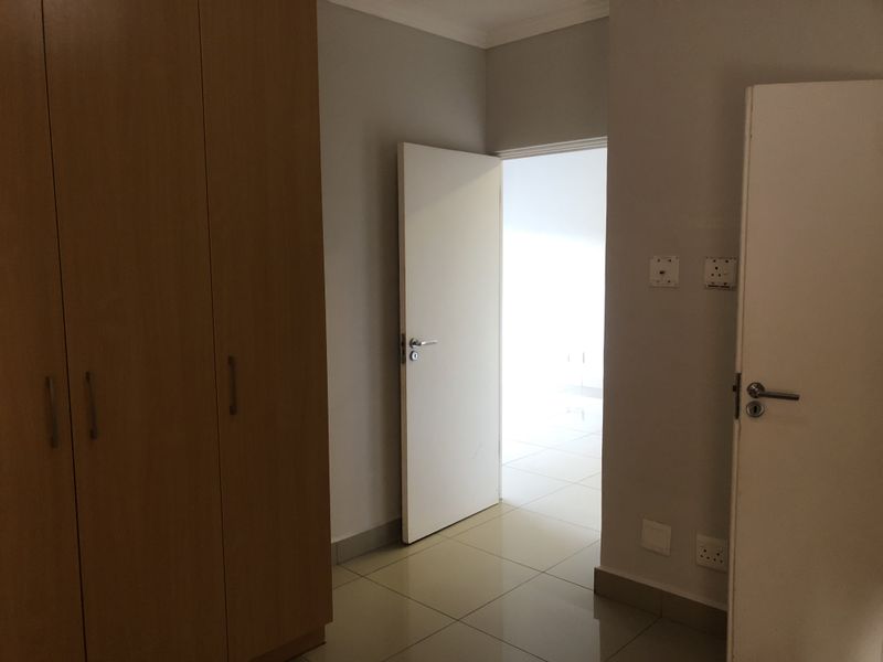 A clean, empty bedroom featuring built-in wooden cupboards, neutral tiled flooring, and a doorway leading to an adjacent space.
