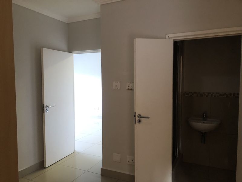 A clean, neutral-toned hallway featuring tiled flooring and access to adjacent rooms, including a bathroom with a wall-mounted basin.