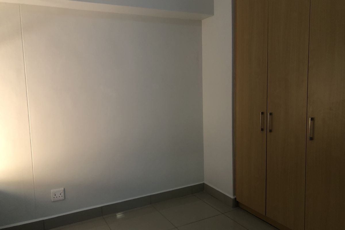 A clean, empty bedroom featuring neutral tiled flooring and built-in wooden cupboards, providing a versatile space ready for personalization.