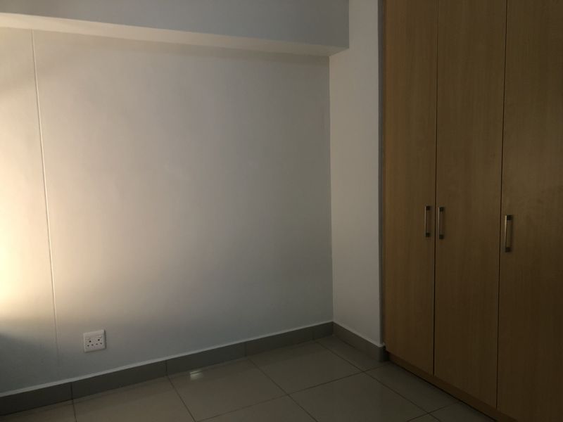 A clean, empty bedroom featuring neutral tiled flooring and built-in wooden cupboards, providing a versatile space ready for personalization.
