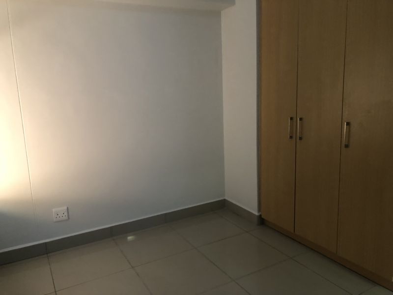 A clean, empty bedroom featuring neutral tiled flooring and a large, built-in wooden wardrobe.