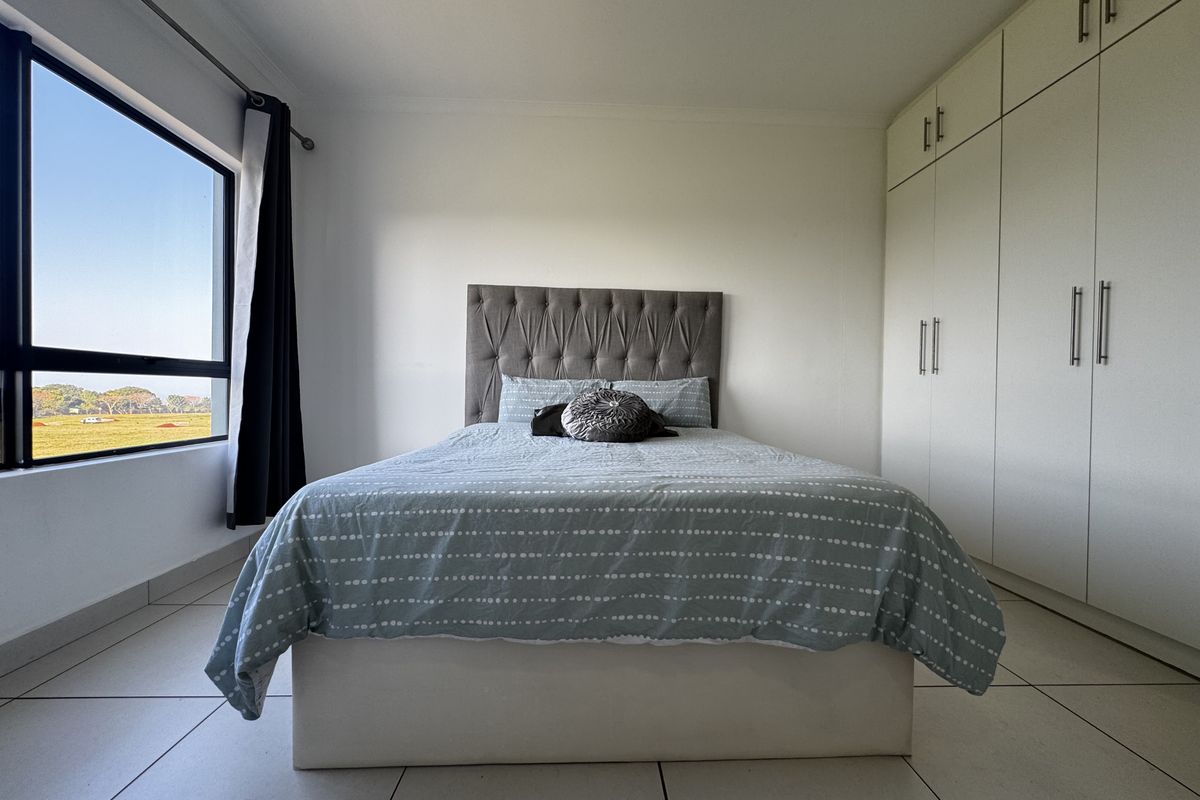 A bright bedroom featuring neutral tiled flooring, ample built-in cupboard storage, and a large window offering natural light and scenic views.