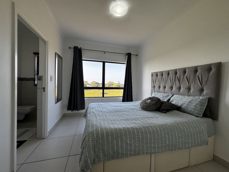 A well-lit bedroom featuring tiled flooring, a large window with natural light, and direct access to an en-suite bathroom.