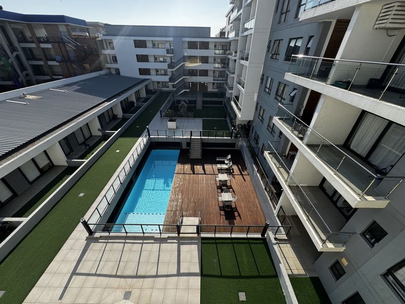 Elevated view of a modern apartment complex courtyard featuring a swimming pool, timber deck, and landscaped artificial lawn areas.