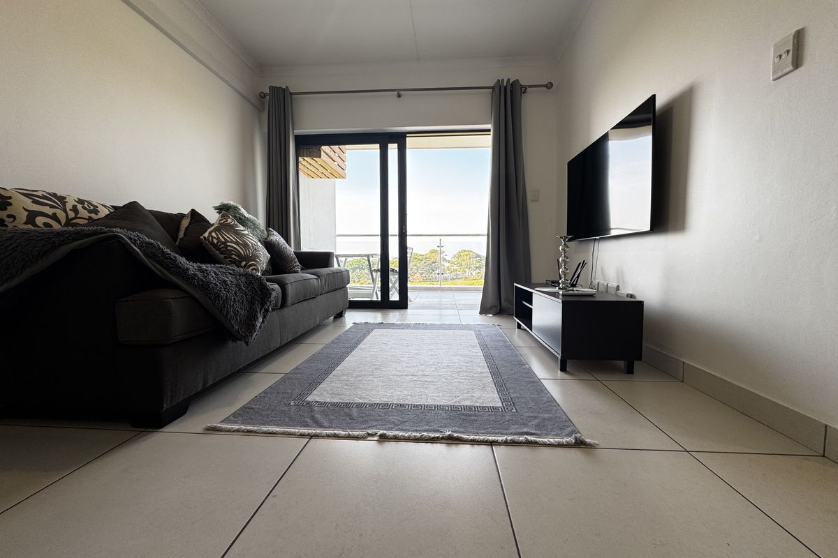 A bright living room featuring neutral tiled flooring, cove cornicing, and a large sliding glass door providing access to an outdoor balcony area.