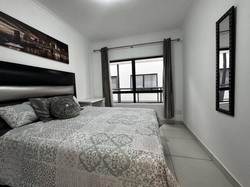 A well-maintained bedroom featuring neutral tiled flooring, clean white walls, and a large window with an aluminium frame.