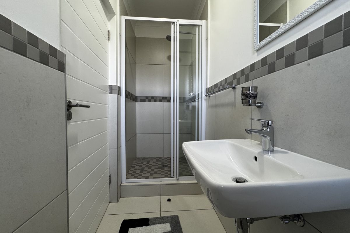 A clean, modern bathroom featuring a glass-enclosed shower, wall-mounted basin with chrome fixtures, and neutral tiled finishes.