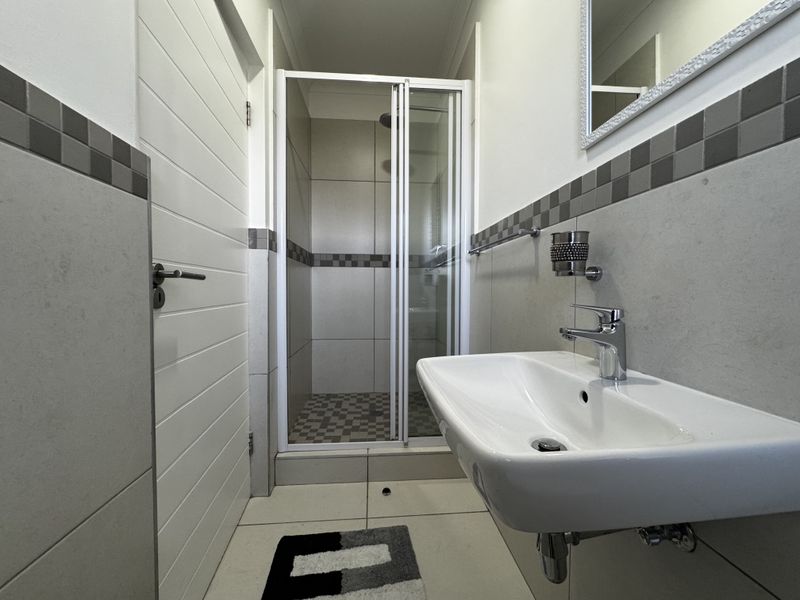 A clean, modern bathroom featuring a glass-enclosed shower, wall-mounted basin with chrome fixtures, and neutral tiled finishes.