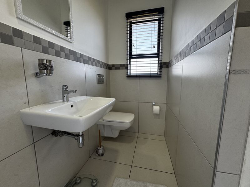 A modern, compact bathroom featuring a wall-mounted basin, wall-hung toilet, and neutral tiled finishes with a window for natural light.
