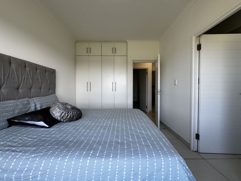 A well-maintained bedroom featuring built-in cupboards, neutral tiled flooring, and clean white walls, providing a functional and bright living space.