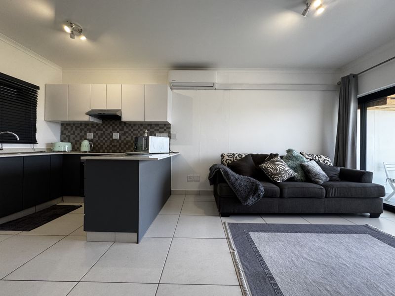 Modern open-plan living area featuring a contemporary kitchen with dark lower cabinets, white upper units, tiled backsplash, and a split-system air conditioner.