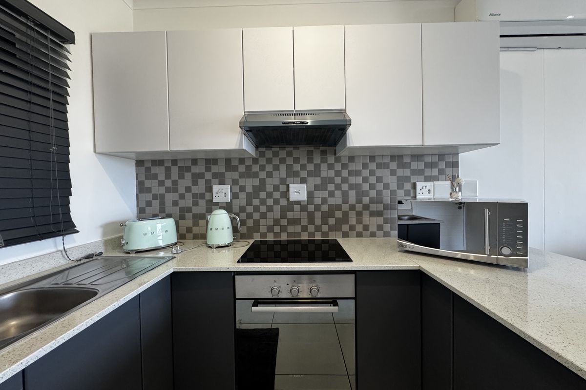 Modern kitchen featuring dark lower cabinetry, white upper cabinets, stone countertops, electric hob, built-in oven, and a tiled splashback.