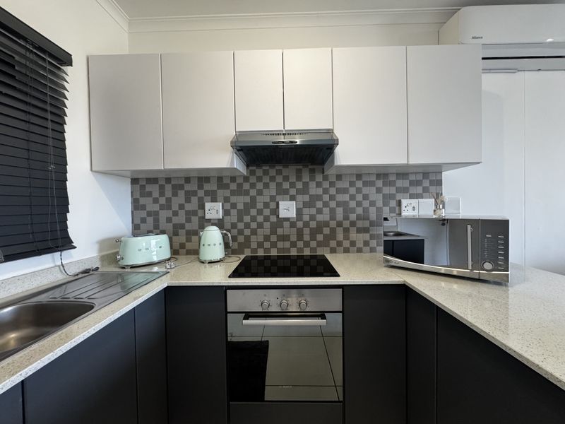 Modern kitchen featuring dark lower cabinetry, white upper cabinets, stone countertops, electric hob, built-in oven, and a tiled splashback.