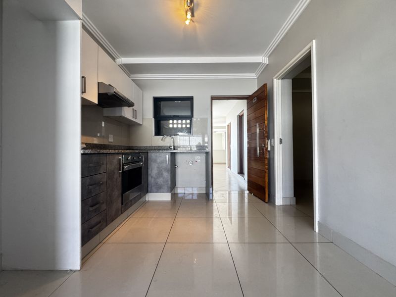 Modern kitchen featuring sleek dark cabinetry, granite countertops, integrated oven, and extractor fan, complemented by neutral tiled flooring and clean finishes.