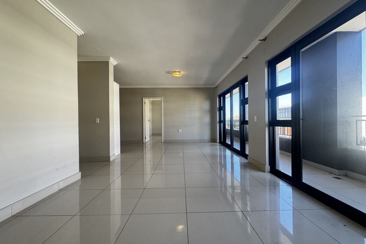 Spacious, empty living area featuring polished porcelain floor tiles, crown molding, and large sliding glass doors providing access to the balcony.