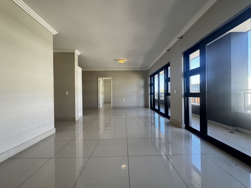 Spacious, empty living area featuring polished porcelain floor tiles, crown molding, and large sliding glass doors providing access to the balcony.