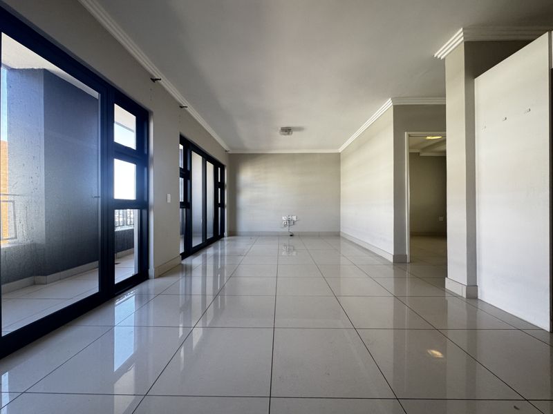 A spacious, empty living area featuring neutral tiled flooring, modern cove cornicing, and large sliding glass doors providing access to an outdoor balcony.