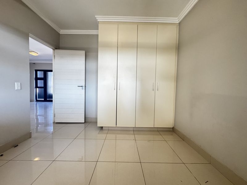 A bright, empty bedroom featuring neutral tiled flooring, built-in cupboards, and decorative ceiling cornicing, offering a clean and versatile living space.