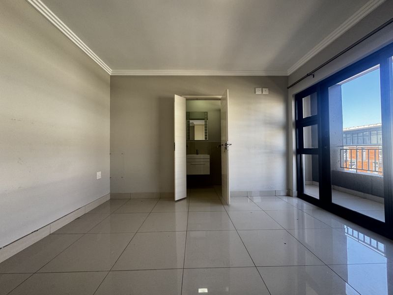 An empty bedroom featuring tiled flooring, a sliding glass door leading to a balcony, and direct access to an en-suite bathroom.