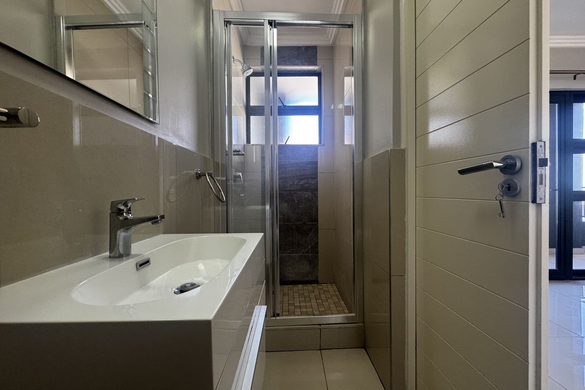 A modern, well-maintained bathroom featuring a sleek vanity basin, a glass-enclosed shower, and neutral wall and floor tiling.