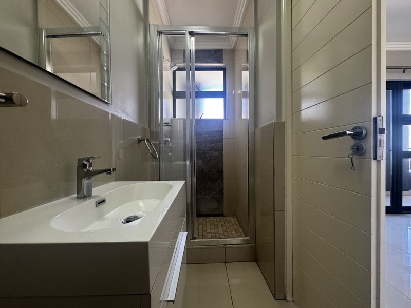 A modern, well-maintained bathroom featuring a sleek vanity basin, a glass-enclosed shower, and neutral wall and floor tiling.