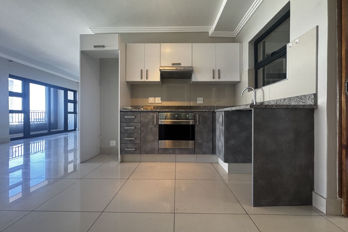 Modern kitchen featuring granite countertops, built-in oven, extractor fan, and sleek two-tone cabinetry, seamlessly integrated into an open-plan living space.