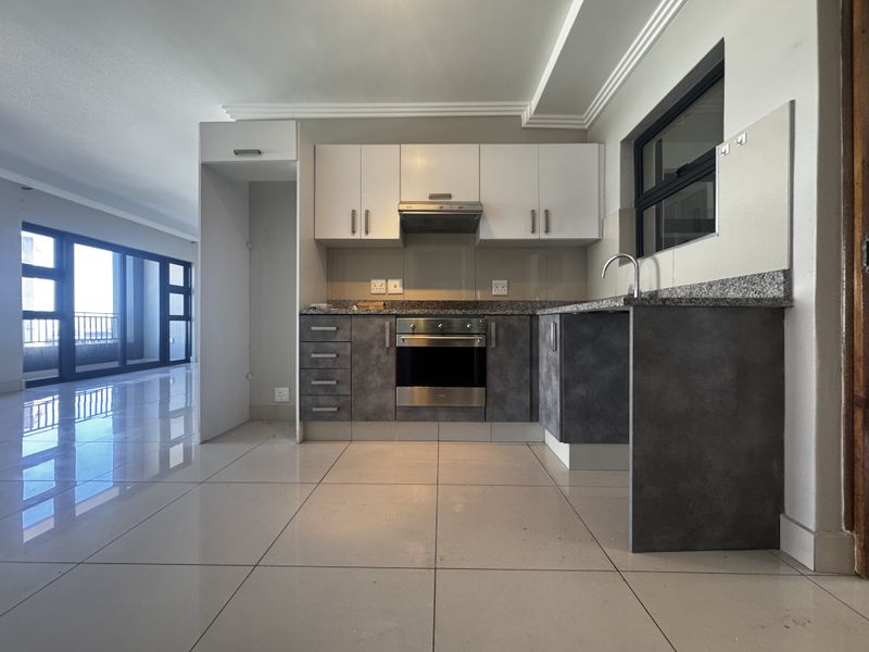 Modern kitchen featuring granite countertops, built-in oven, extractor fan, and sleek two-tone cabinetry, seamlessly integrated into an open-plan living space.