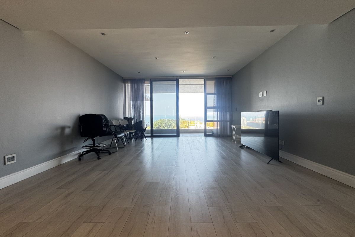Spacious living area featuring modern laminate flooring, recessed lighting, and large sliding glass doors that open to an outdoor balcony with scenic views.