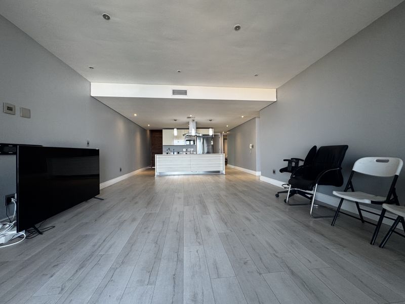 Spacious open-plan living area featuring modern laminate flooring, recessed lighting, and a central kitchen island with integrated cabinetry and extractor fan.
