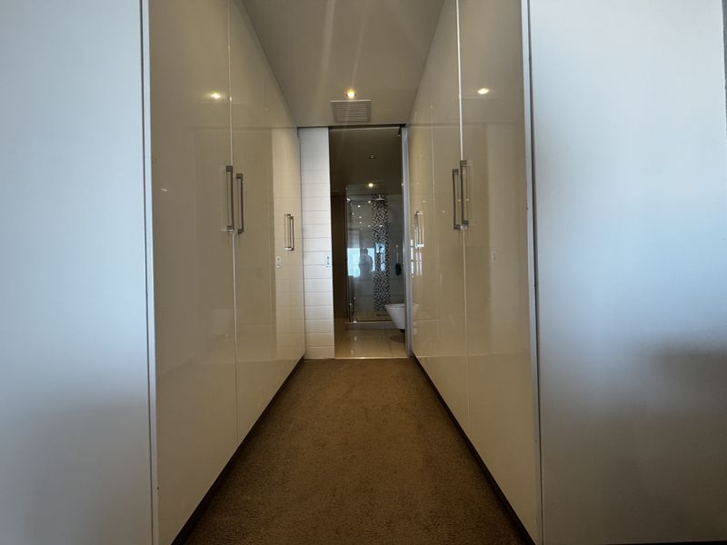 A clean hallway featuring extensive built-in white cabinetry with modern handles, leading directly into a tiled bathroom area.