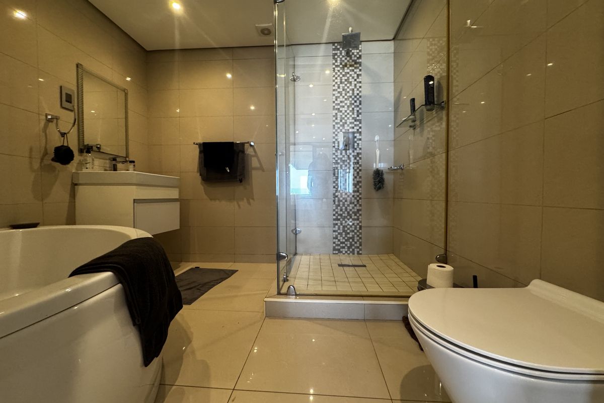 Modern bathroom featuring a glass-enclosed shower, wall-mounted vanity, freestanding bathtub, and wall-hung toilet with neutral floor-to-ceiling tiling and recessed lighting.