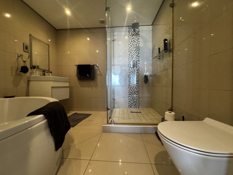 Modern bathroom featuring a glass-enclosed shower, wall-mounted vanity, freestanding bathtub, and wall-hung toilet with neutral floor-to-ceiling tiling and recessed lighting.