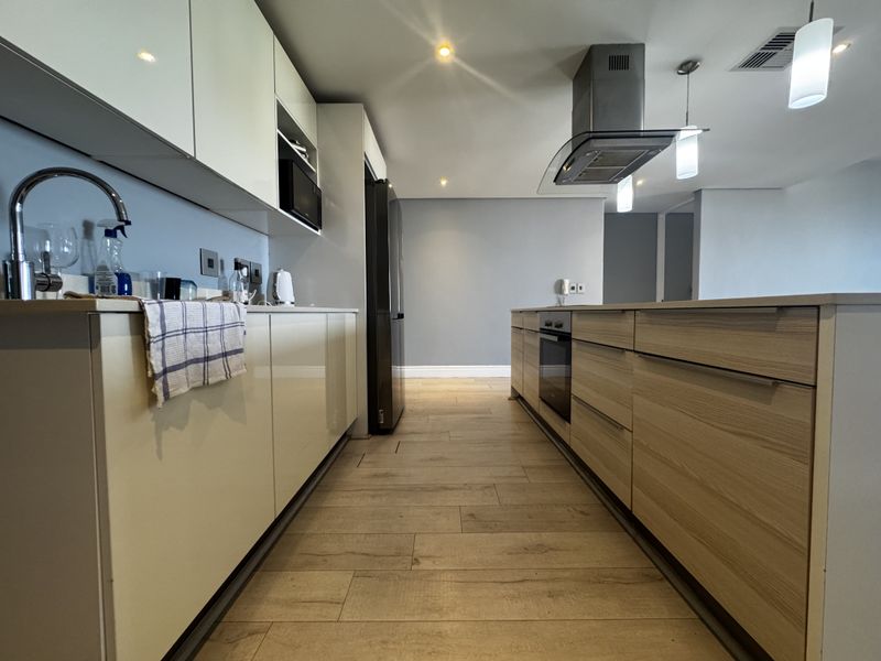 Modern kitchen featuring sleek cabinetry, a central island with built-in oven, stainless steel extractor fan, and durable wood-look tile flooring.