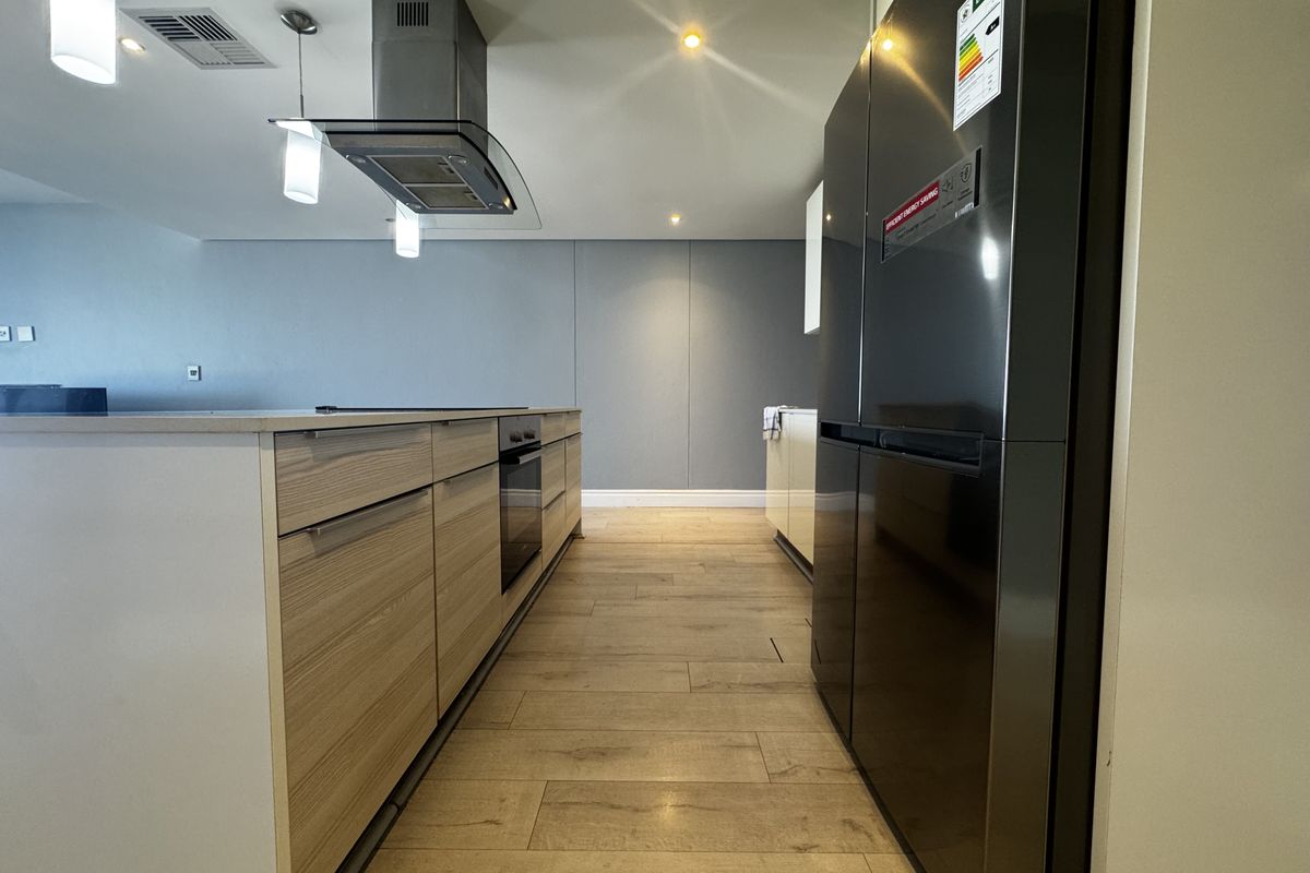 Modern kitchen featuring a central island, built-in oven, stainless steel extractor fan, and contemporary wood-look tile flooring with recessed and pendant lighting.