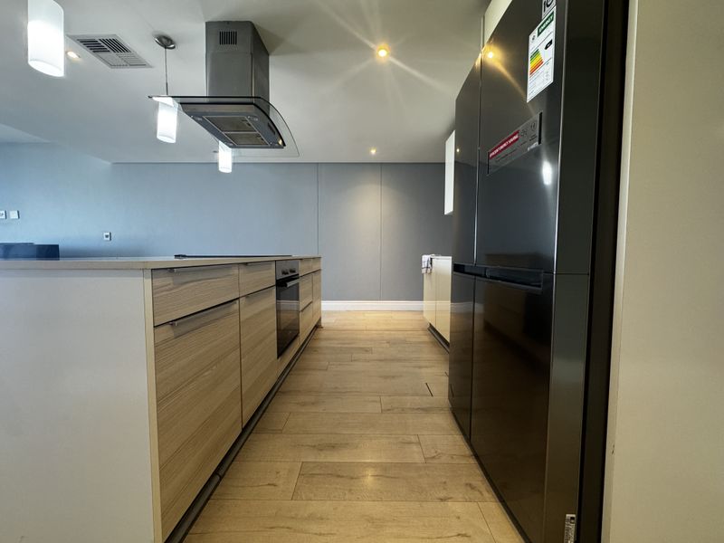 Modern kitchen featuring a central island, built-in oven, stainless steel extractor fan, and contemporary wood-look tile flooring with recessed and pendant lighting.