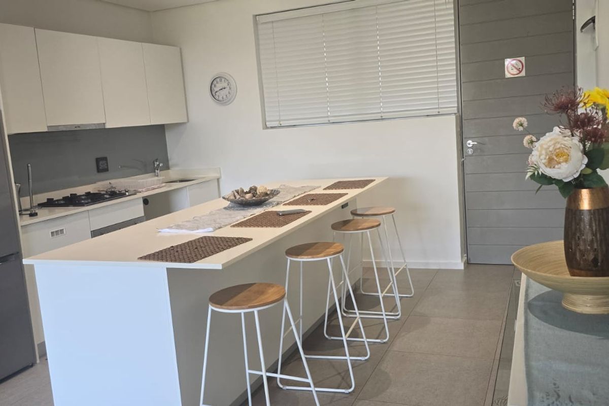 Modern kitchen featuring white cabinetry, a central island with breakfast bar seating, gas hob, and tiled flooring.