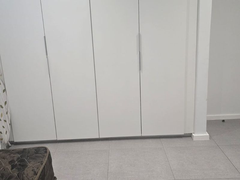 A clean, minimalist bedroom featuring neutral tiled flooring and ample built-in cupboard storage, providing a versatile space ready for personalization.
