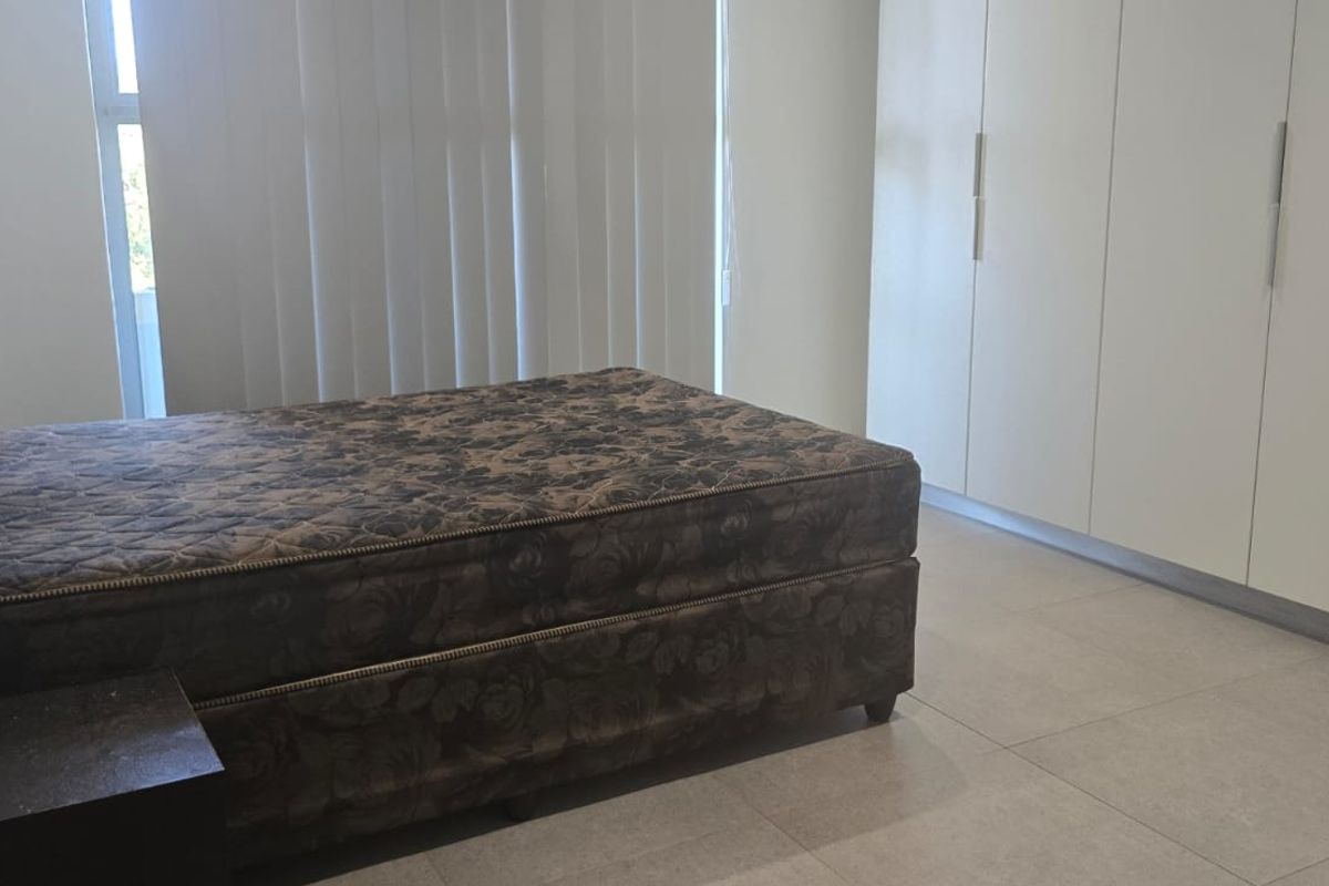A bedroom featuring neutral tiled flooring, ample built-in cupboard storage, and vertical blinds allowing natural light.