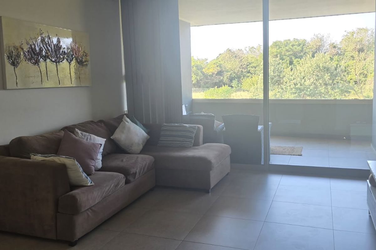 A bright living room featuring large sliding glass doors that open onto a balcony, providing natural light and views of the surrounding greenery.