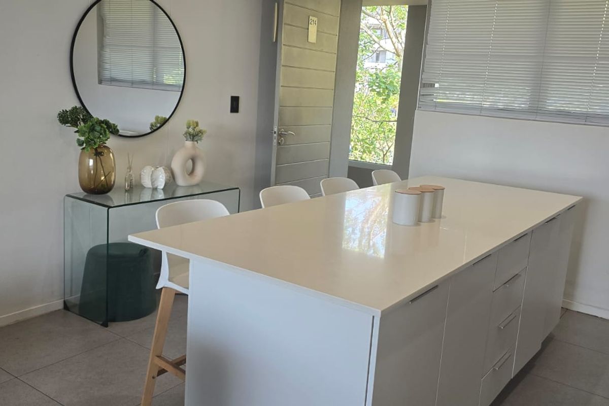 Modern kitchen featuring a central island with a white quartz countertop, sleek cabinetry, and tiled flooring, offering a clean and functional workspace.