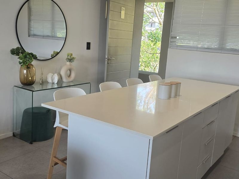 Modern kitchen featuring a central island with a white quartz countertop, sleek cabinetry, and tiled flooring, offering a clean and functional workspace.