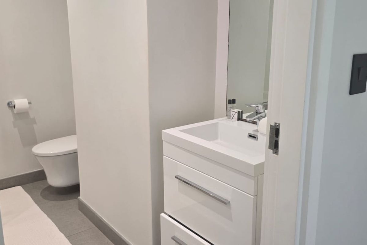 A modern, clean-lined bathroom featuring a sleek vanity cabinet with an integrated sink, a wall-mounted toilet, and neutral floor tiling.