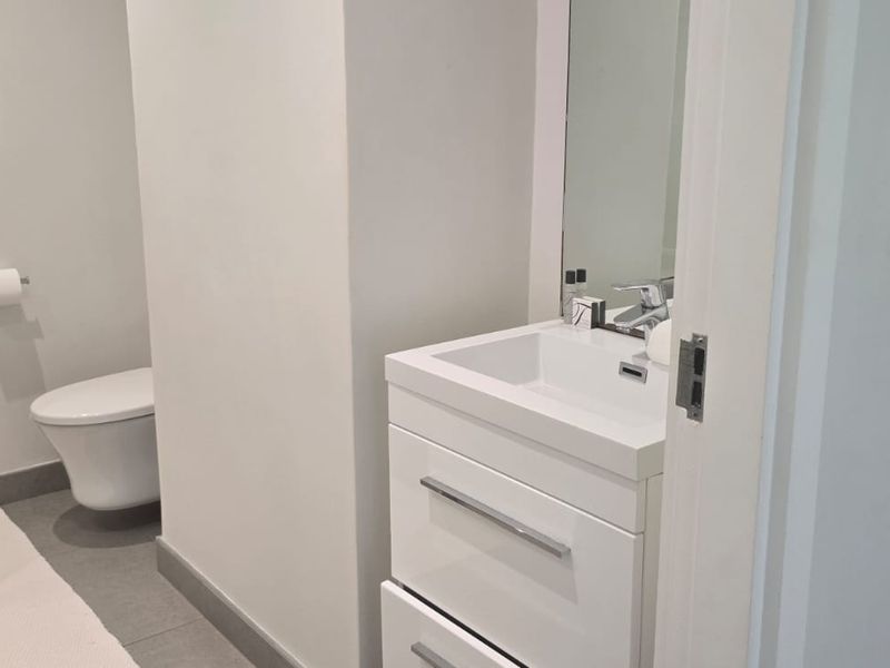 A modern, clean-lined bathroom featuring a sleek vanity cabinet with an integrated sink, a wall-mounted toilet, and neutral floor tiling.