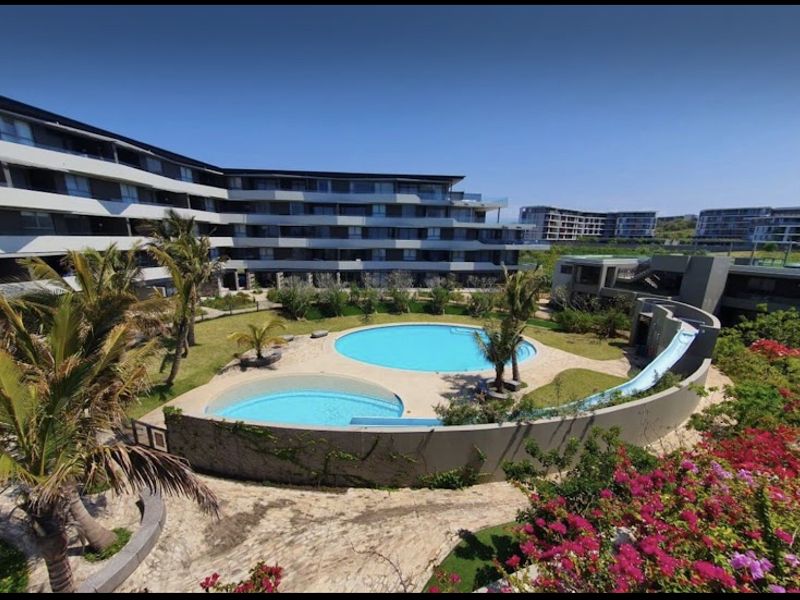 Aerial view of a modern apartment complex featuring a communal swimming pool, water slide, and well-maintained landscaped garden areas.