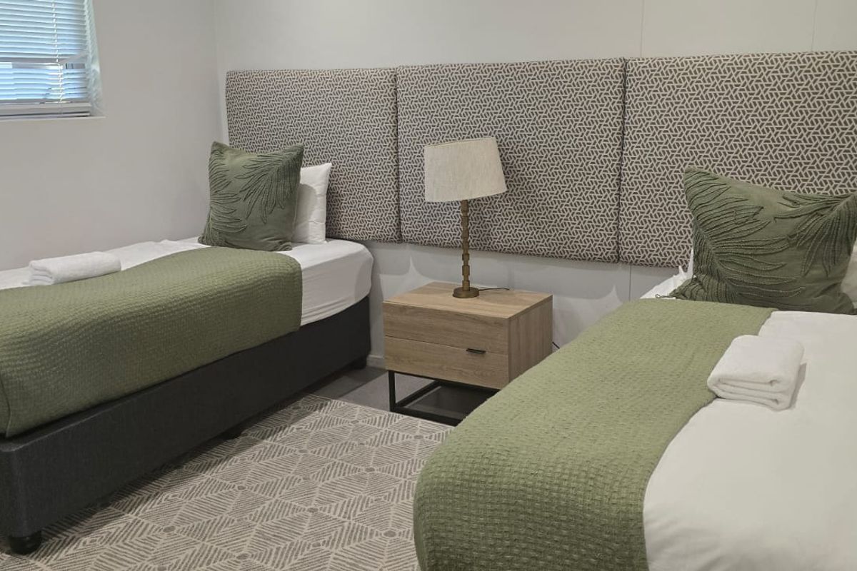 A well-maintained bedroom featuring neutral tones, upholstered wall panels, and venetian blinds, providing a clean and comfortable sleeping space.