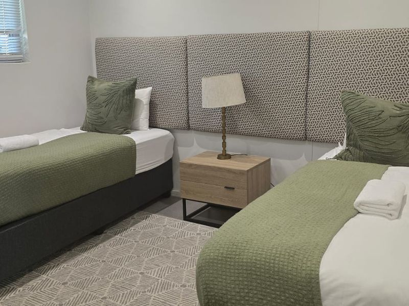 A well-maintained bedroom featuring neutral tones, upholstered wall panels, and venetian blinds, providing a clean and comfortable sleeping space.