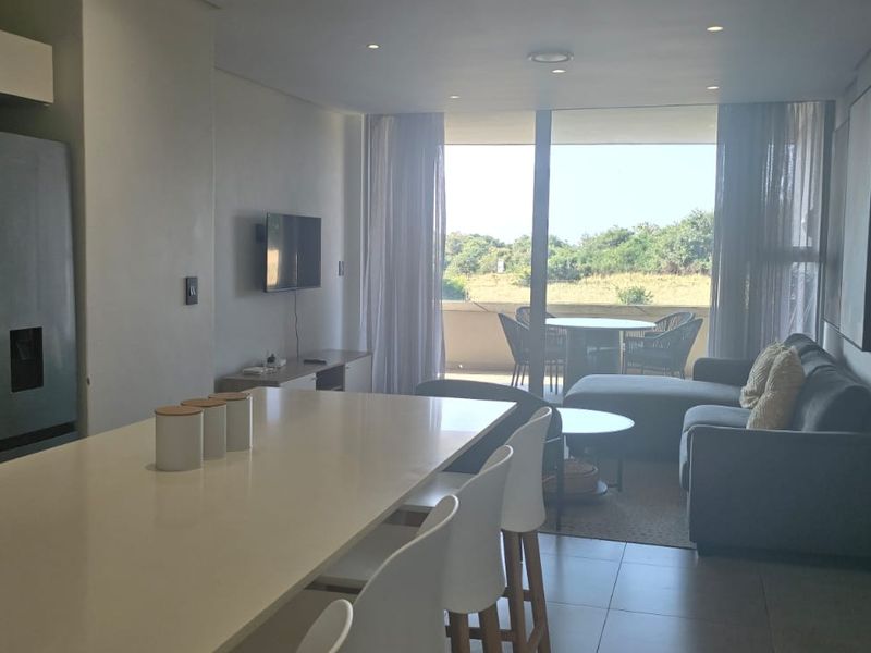 Modern open-plan living area featuring a sleek kitchen island, tiled floors, and large sliding doors leading to a balcony with natural light.